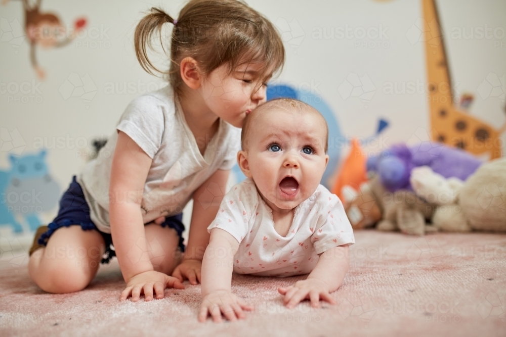 Kiss from big sister whilst baby has tummy time on carpet - Australian Stock Image