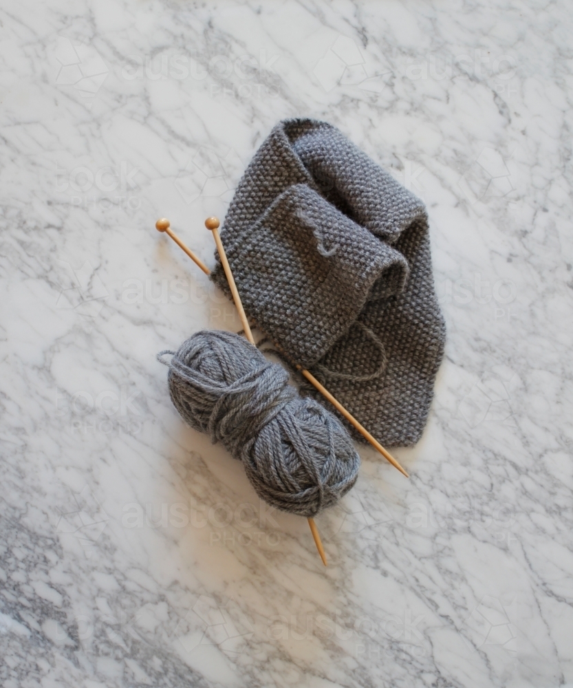 Knitting with wooden knitting needles with grey wool on marble - Australian Stock Image