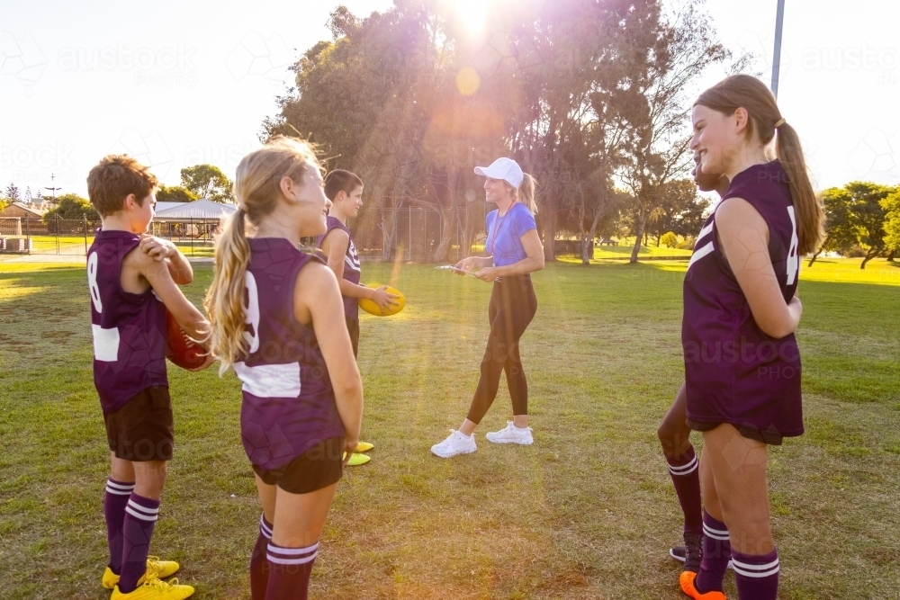 lady coaching kids football team with sun flare - Australian Stock Image