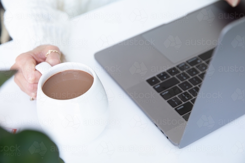 lady's hands typing on laptop with white hug mug in the foreground - Australian Stock Image