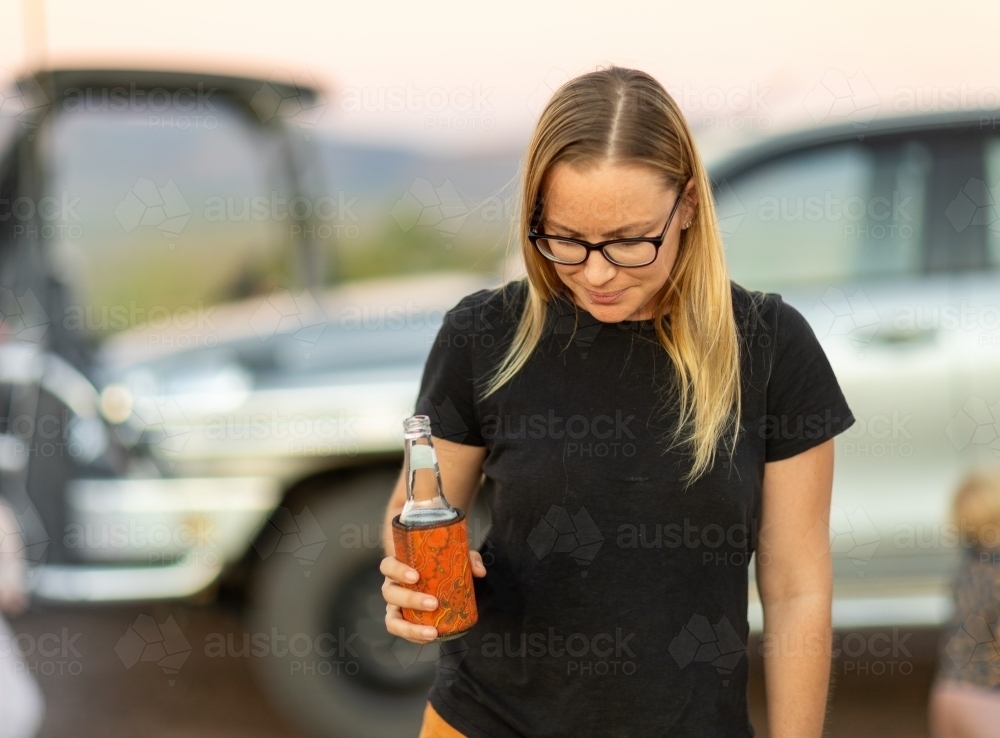 lady with beer in hand and blurry vehicle in background - Australian Stock Image