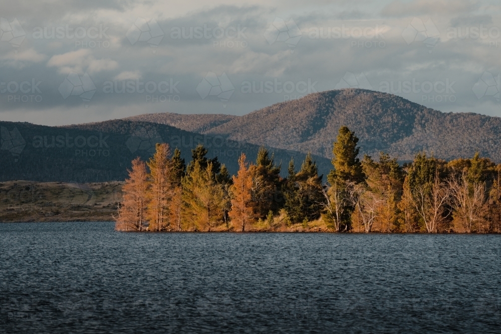 Lake Jindabyne at sunset with autumn coloured trees and mountains - Australian Stock Image