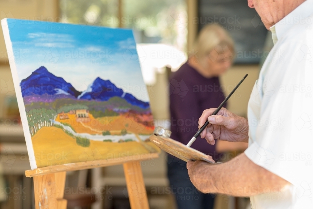 Landscape painting on easel with man holding paintbrush and palette - Australian Stock Image