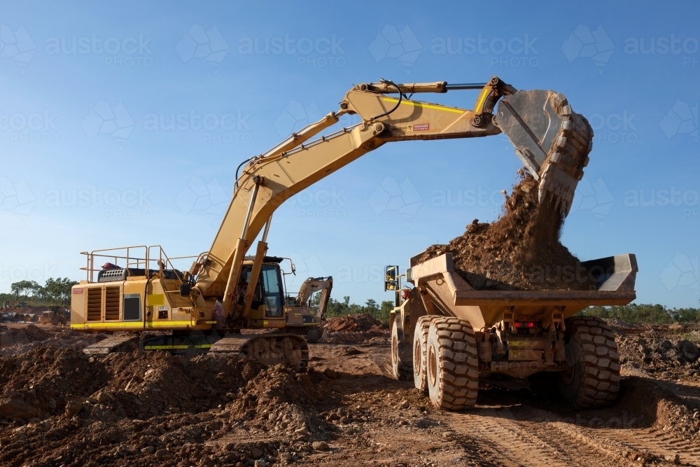 Large digger moving dirt into an earth mover on an industrial building site - Australian Stock Image