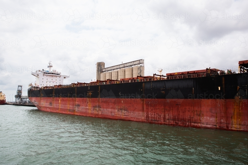 large red and black ship docked next to silos in Gladstone - Australian Stock Image