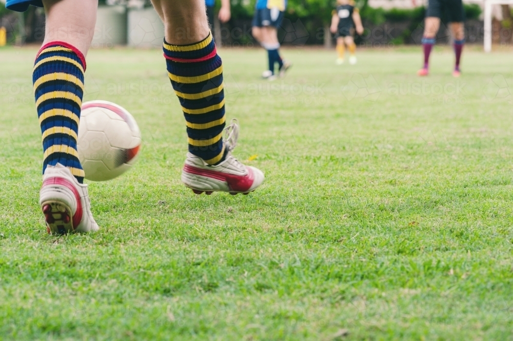 Legs of a man kicking a ball during a soccer game - Australian Stock Image