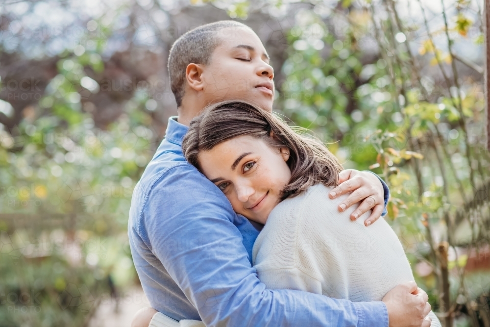 lgbtqi couple being cozy outside with one looking at the camera - Australian Stock Image