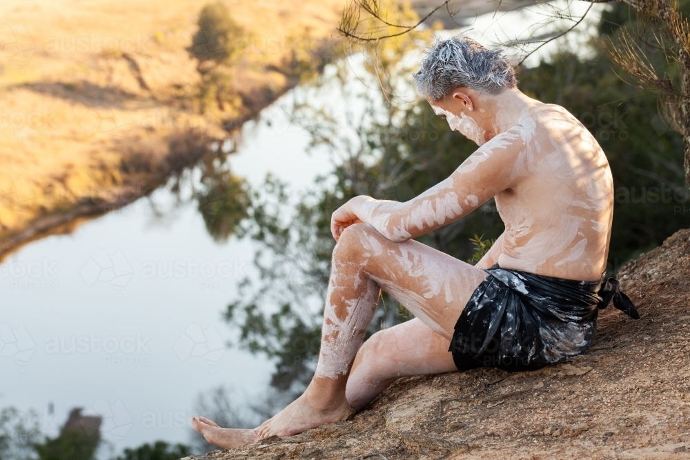 Light skinned aboriginal young man sitting on cliff edge in Wonnarua country - Australian Stock Image