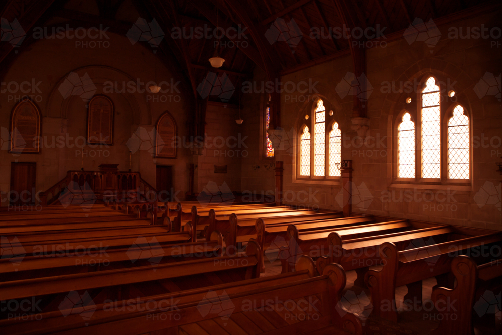 Light streams through a stained glass window onto pews in an old church in Ross, Tasmania - Australian Stock Image