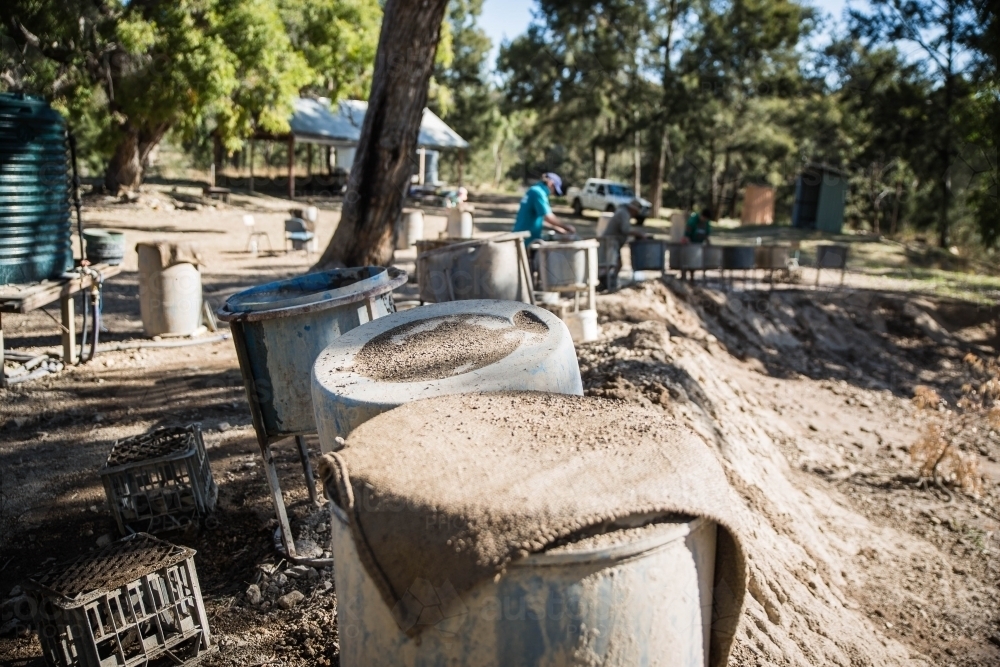 Line of fossicking drums and tubs with dirt and trees - Australian Stock Image