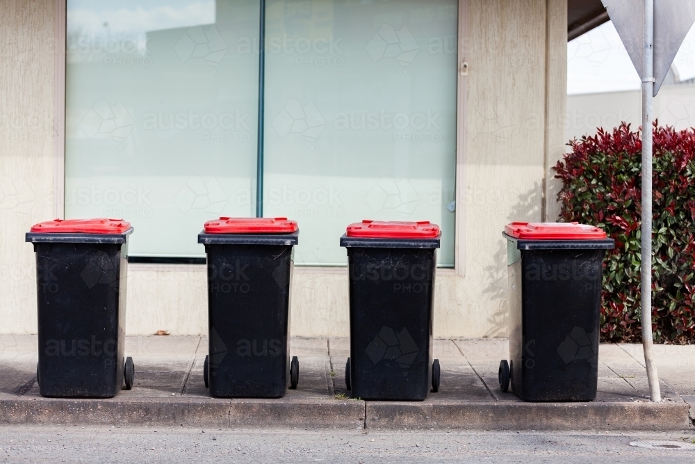 Line of four red lid rubbish bins on urban roadside - Australian Stock Image