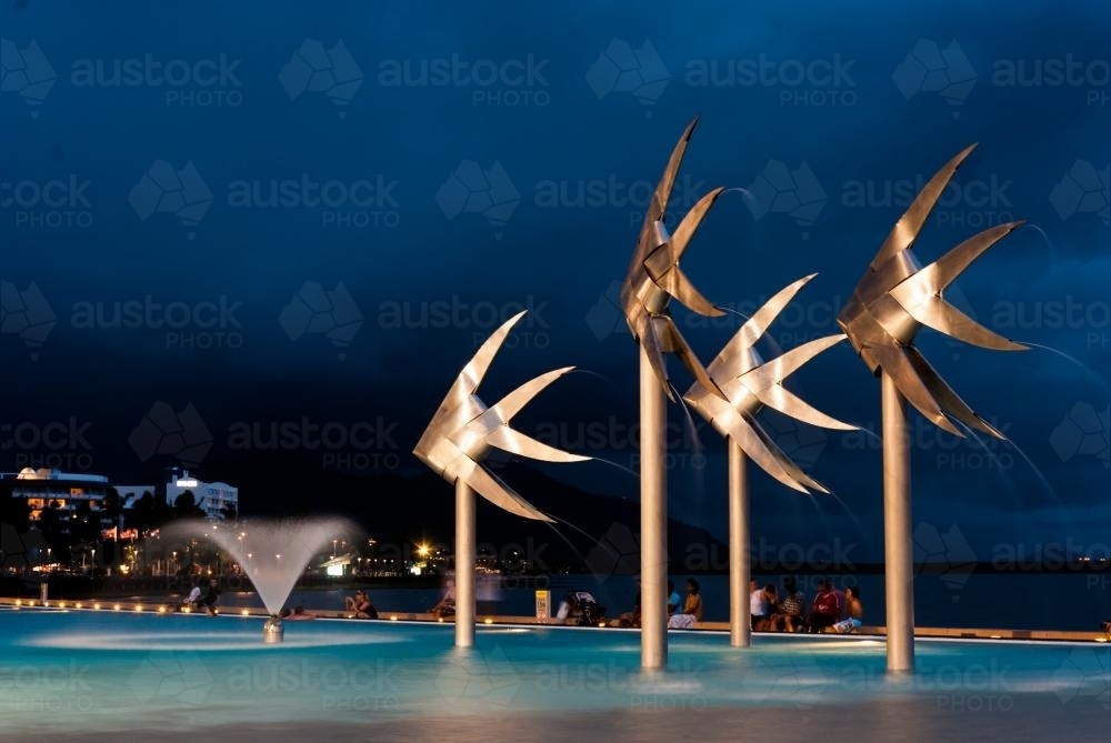 Lit up Sunfish statues and fountain in public pool on foreshore with people in background - Australian Stock Image