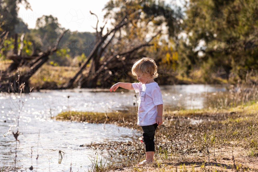 little barefoot aussie boy by the river throwing sticks in water - Australian Stock Image
