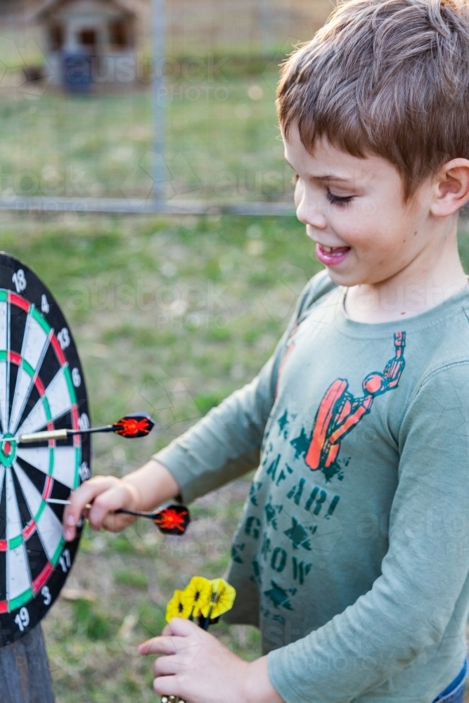 Little boy playing with throwing darts outside - Australian Stock Image