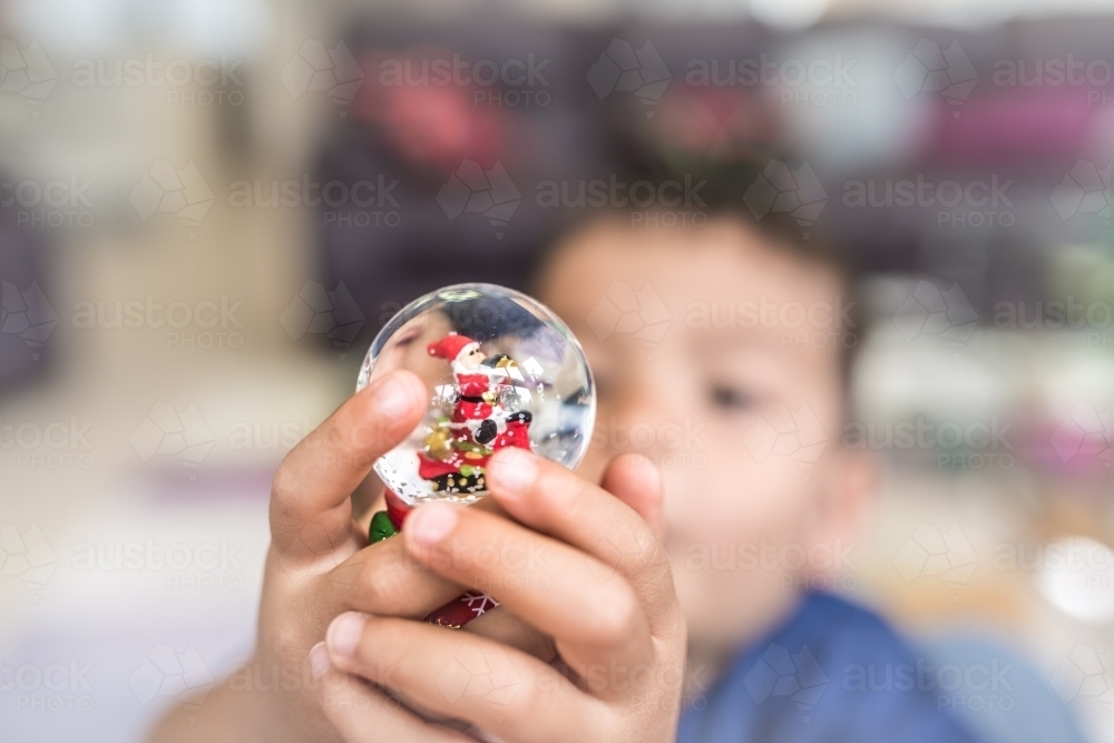 Little boy plays with a Christmas snow globe at his father's feet - Australian Stock Image