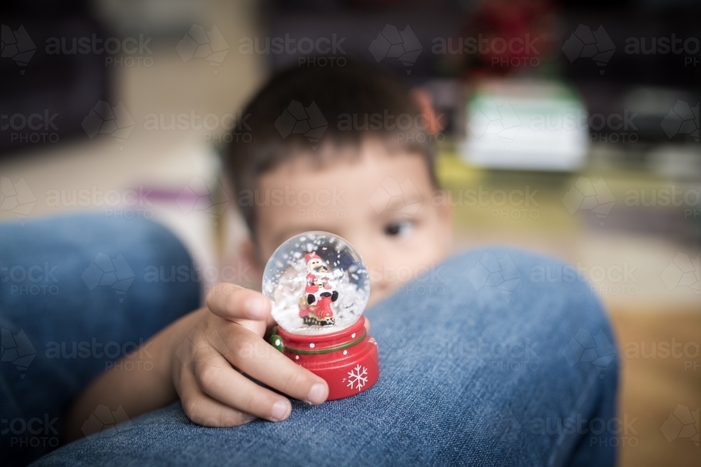 Little boy plays with a Christmas snow globe at his father's feet - Australian Stock Image