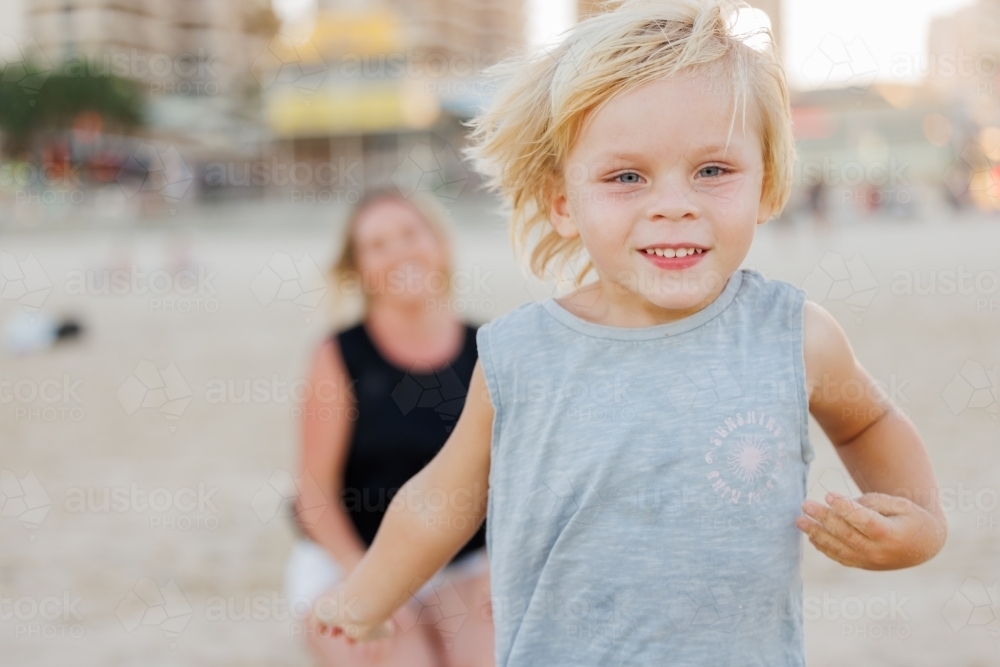 Little boy running on the beach with mother in background - Australian Stock Image