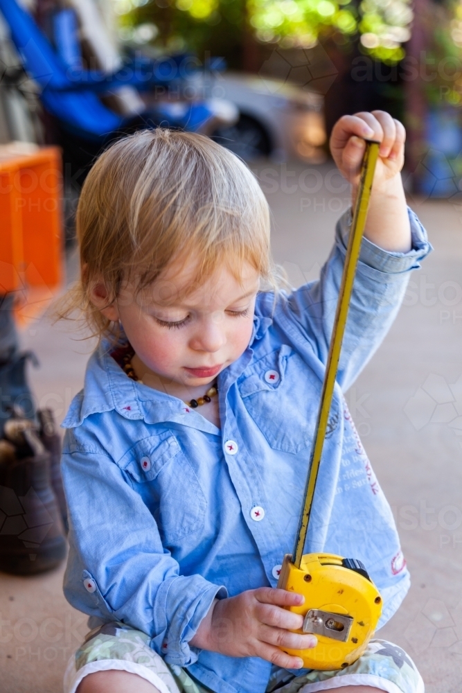Little boy with yellow tape measure measuring how high he is - Australian Stock Image
