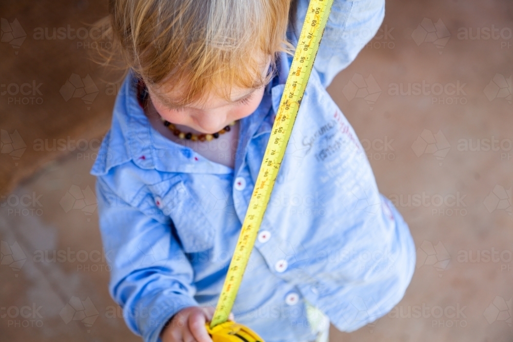 Little boy with yellow tape measure measuring how high he is - Australian Stock Image
