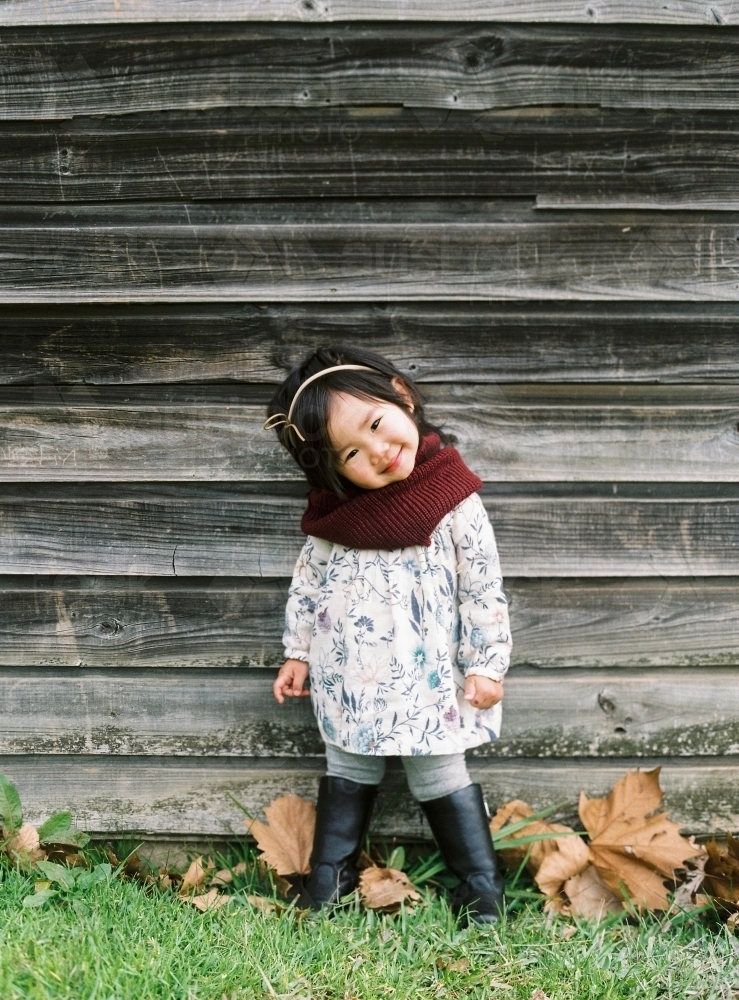 Asian toddler girl standing against rustic farm shed wall - Australian Stock Image