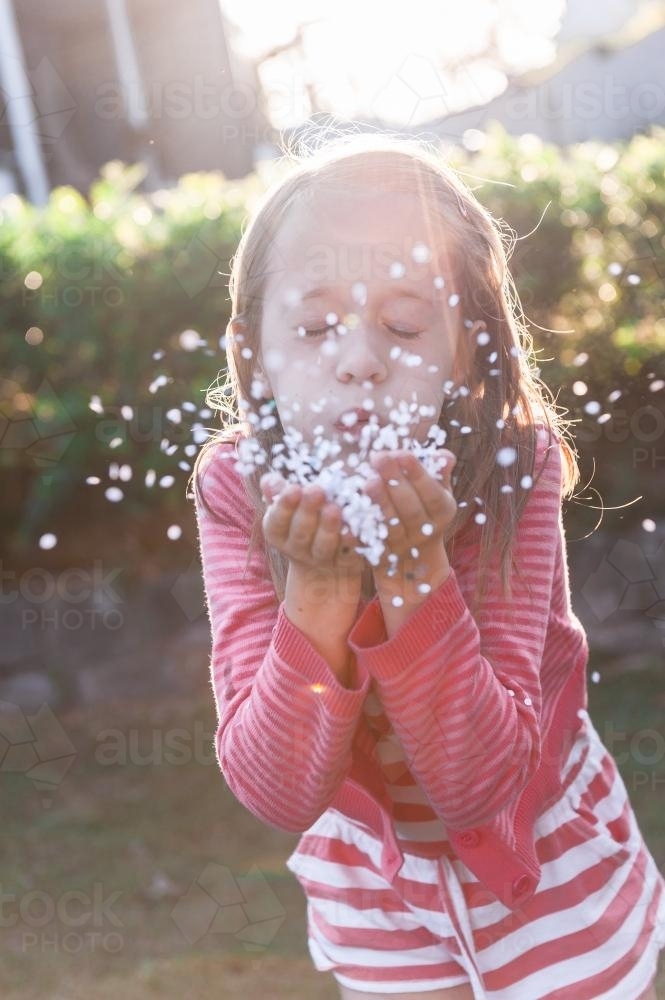 little girl blowing confetti from her hands - Australian Stock Image