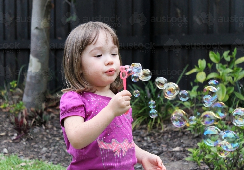 Little girl blowing soap bubbles in backyard garden - Australian Stock Image