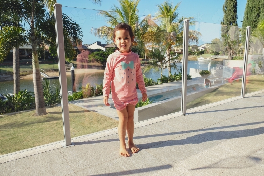 Little girl by pool glass fencing - Australian Stock Image