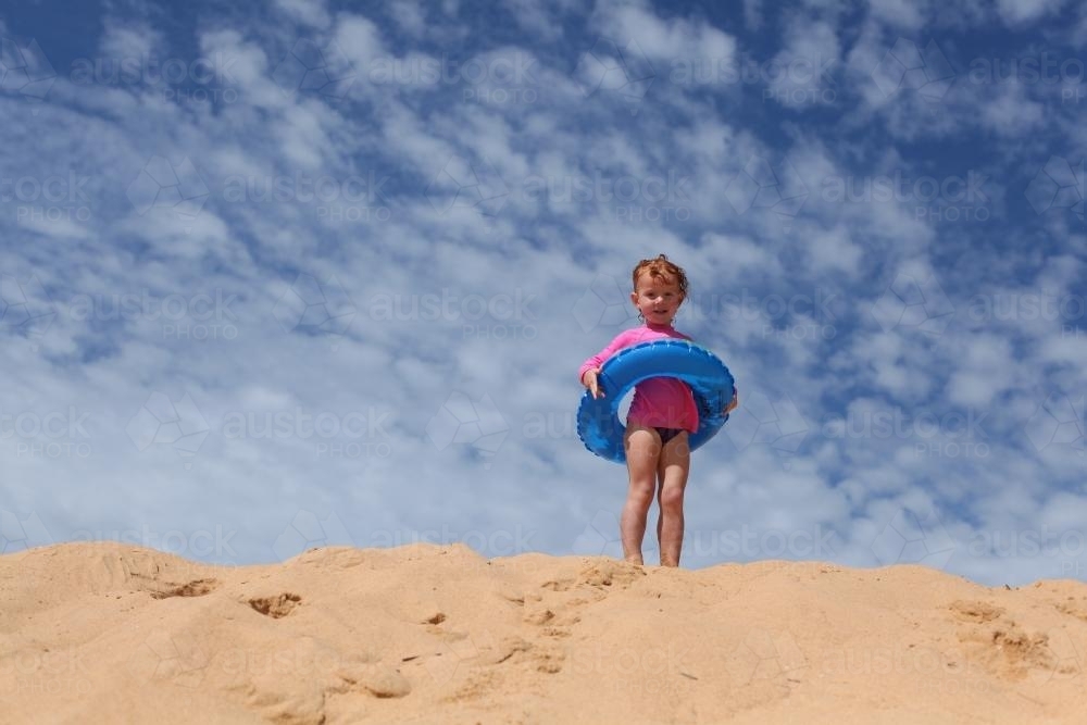 Little girl climbing a sanddune with an inflatable ring - Australian Stock Image