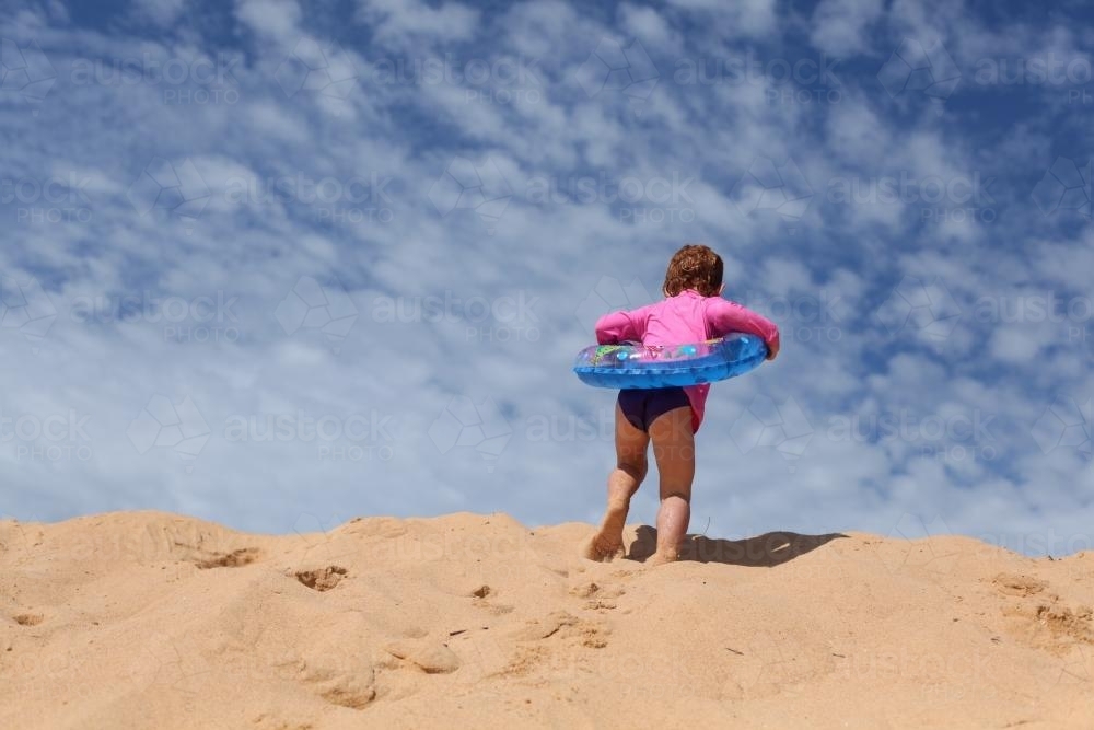 Little girl climbing a sanddune with an inflatable ring - Australian Stock Image