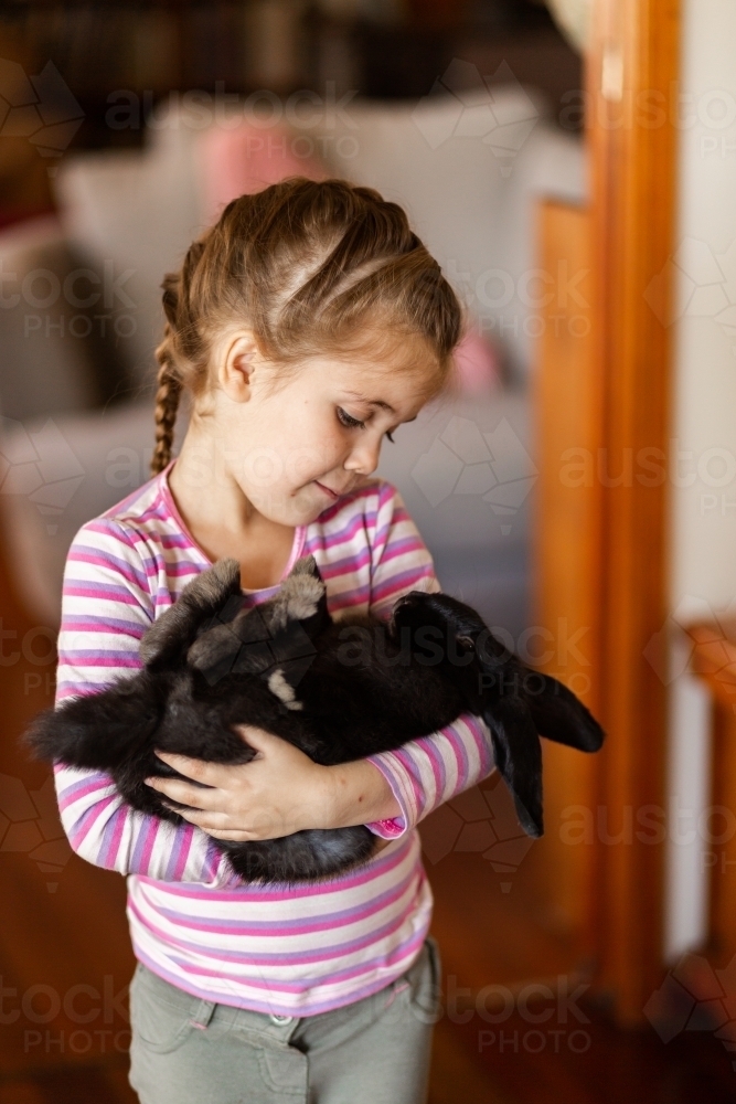 Little girl cuddling with her pet bunny rabbit inside - Australian Stock Image