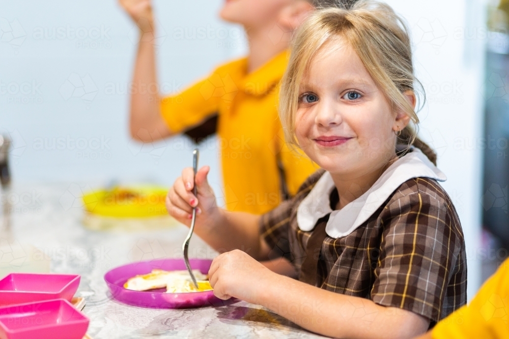 Little girl eating eggs for breakfast before school - Australian Stock Image