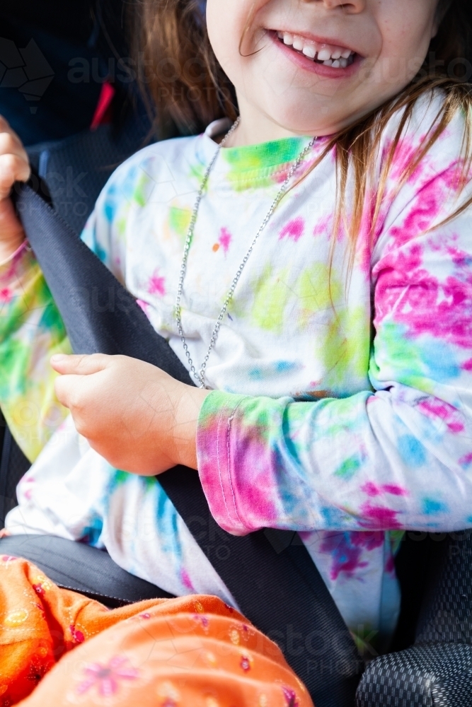 Little girl happily wearing seat belt in booster seat in car - Australian Stock Image