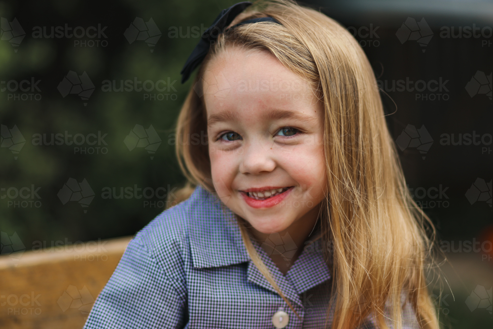 Little girl in school uniform sitting at desk outdoors smiling - Australian Stock Image