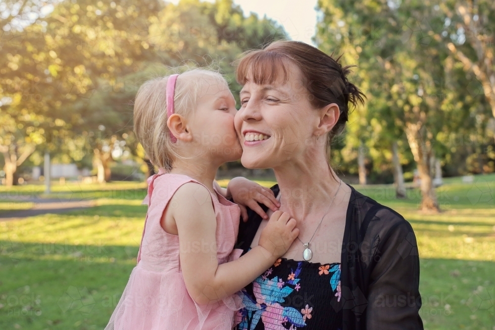 Little girl kissing her mother in the park - Australian Stock Image