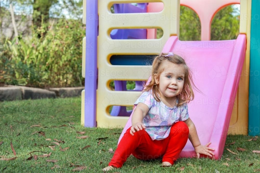 Little girl playing on a plastic play castle and slide - Australian Stock Image