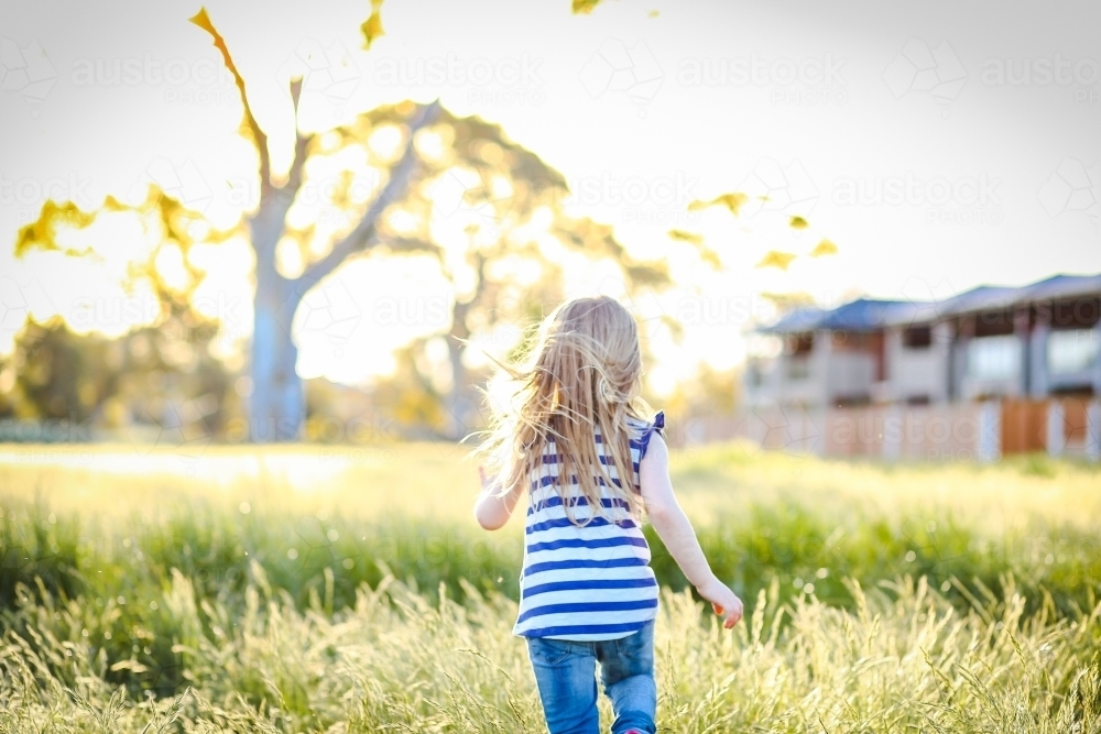 little girl running away through field in golden afternoon light - Australian Stock Image