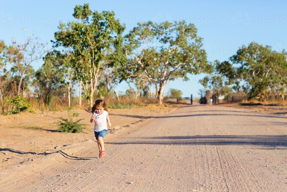 Little girl running down a dirt road driveway - Australian Stock Image