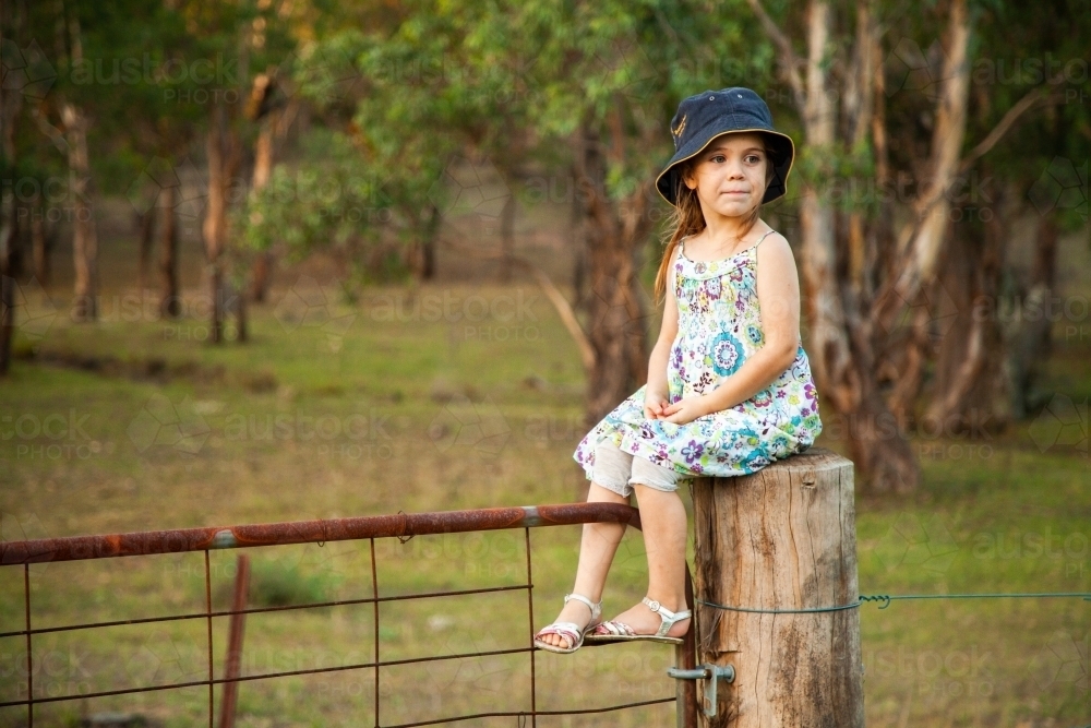 Little girl sitting on gate fence post - Australian Stock Image