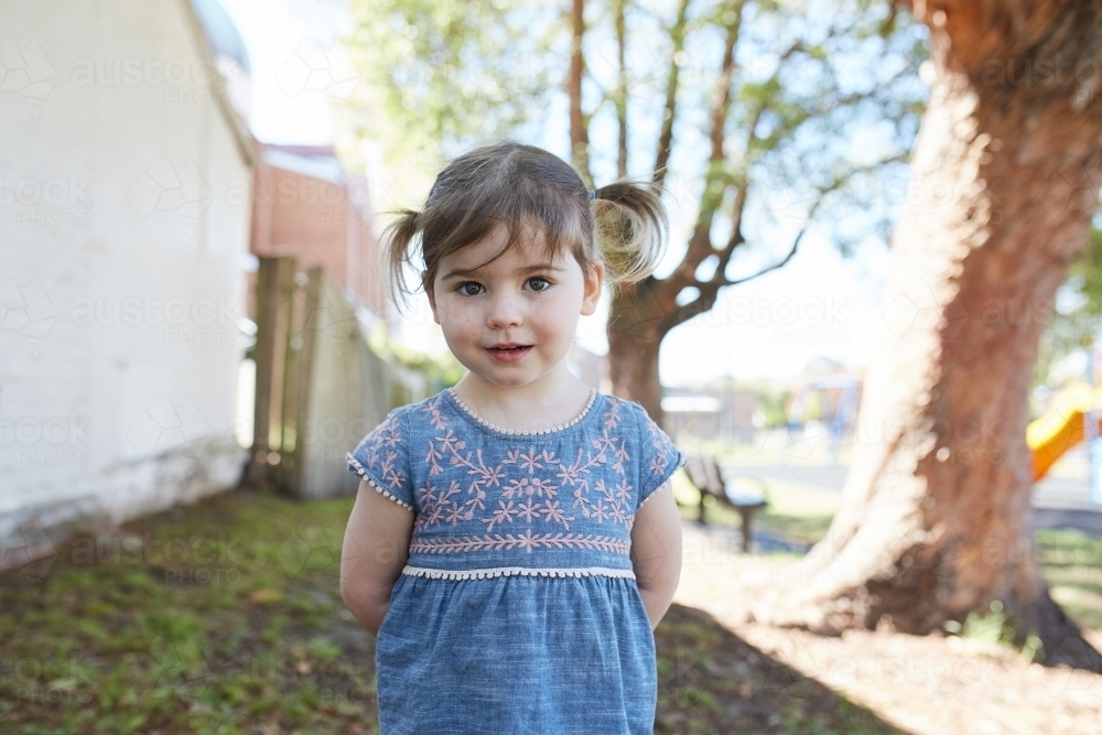 Little girl smiling for camera in inner city park - Australian Stock Image