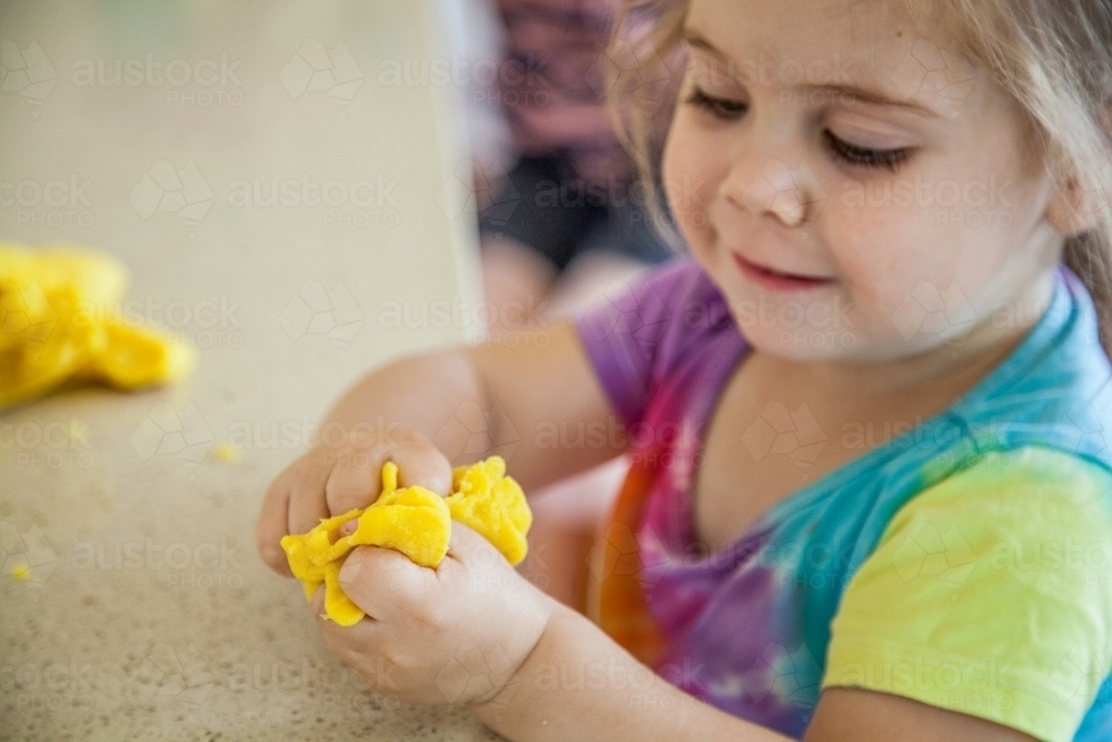 Little girl squishing playdough in her fingers - Australian Stock Image