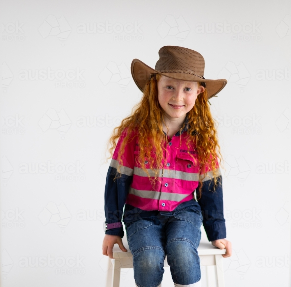 little girl wearing hi-vis shirt and hat against plain white background - Australian Stock Image