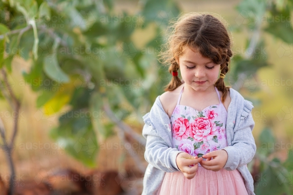 little girl wearing pink floral dress self-absorbed in the outdoors - Australian Stock Image