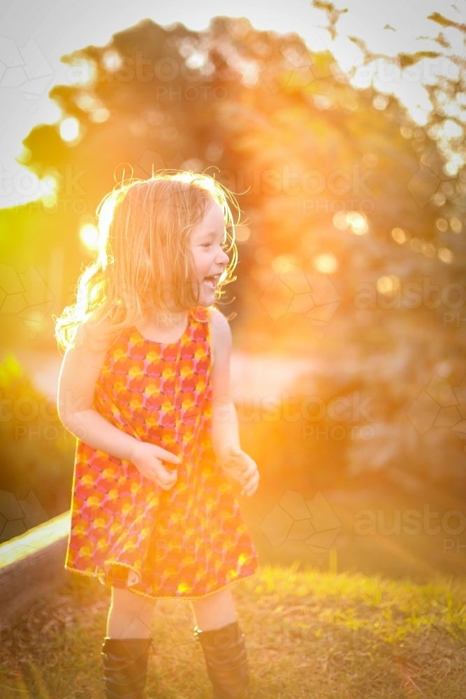 Little girl wearing red dress exploring garden flooded in golden afternoon light - Australian Stock Image