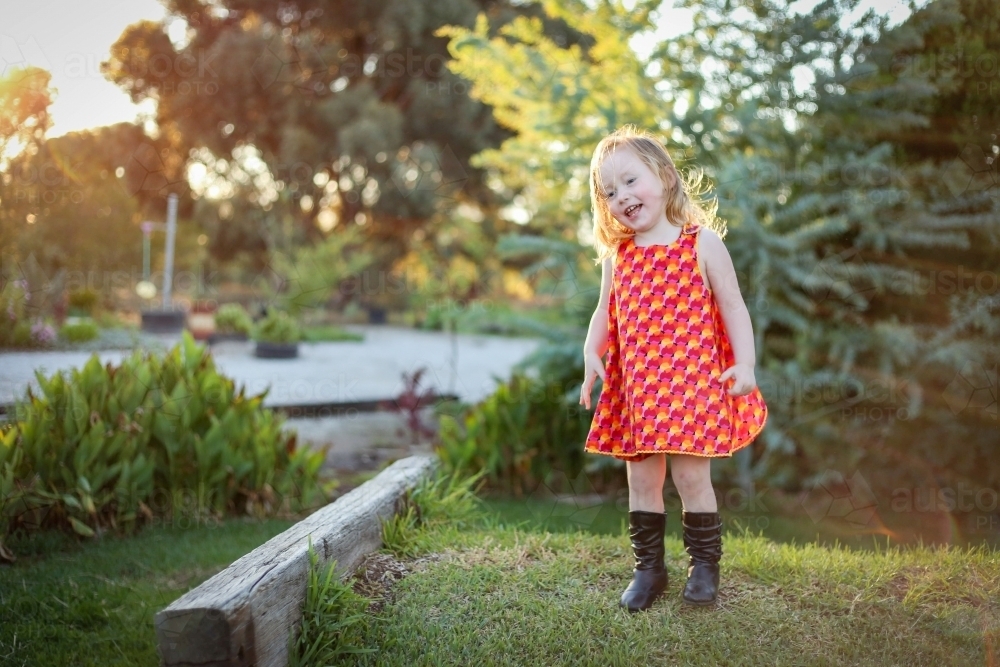 Little girl wearing red dress exploring lush green garden - Australian Stock Image