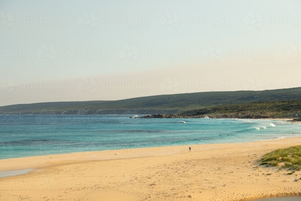 Loan hiker walking on beach with surfers in water - Australian Stock Image