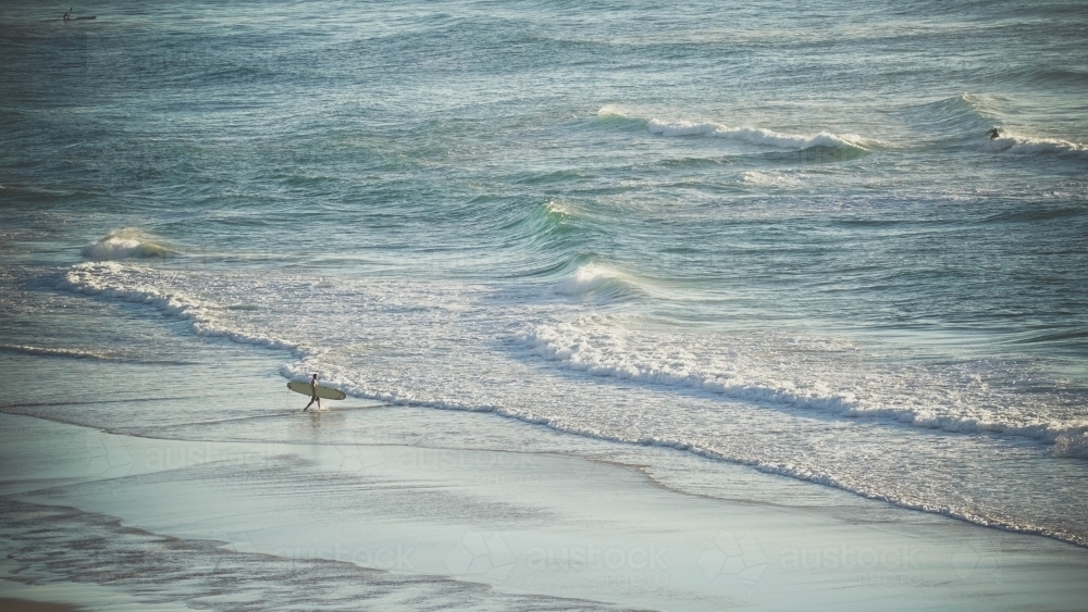 Lone surfer entering water at sunrise - Australian Stock Image