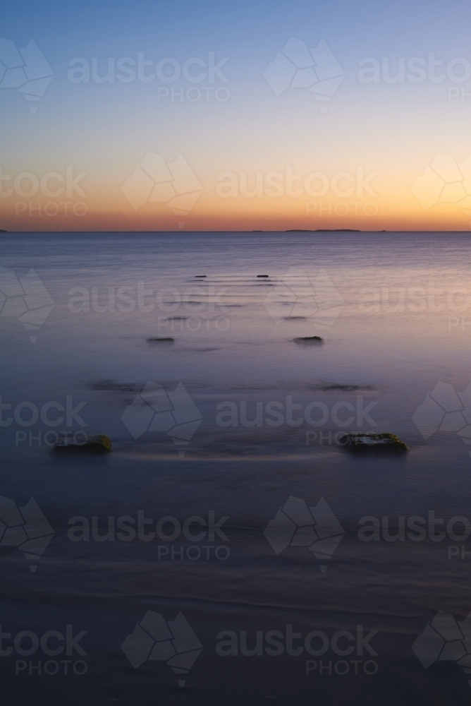 Long exposure of a peaceful ocean at dusk with stumps of an old jetty. - Australian Stock Image