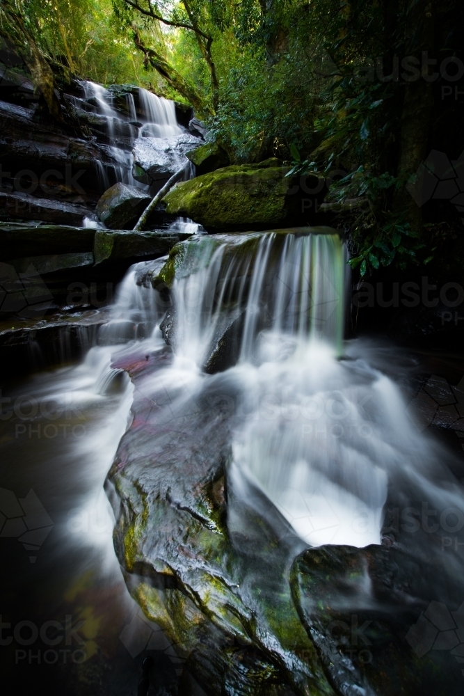 Long exposure of mossy waterfall in dark green forest - Australian Stock Image