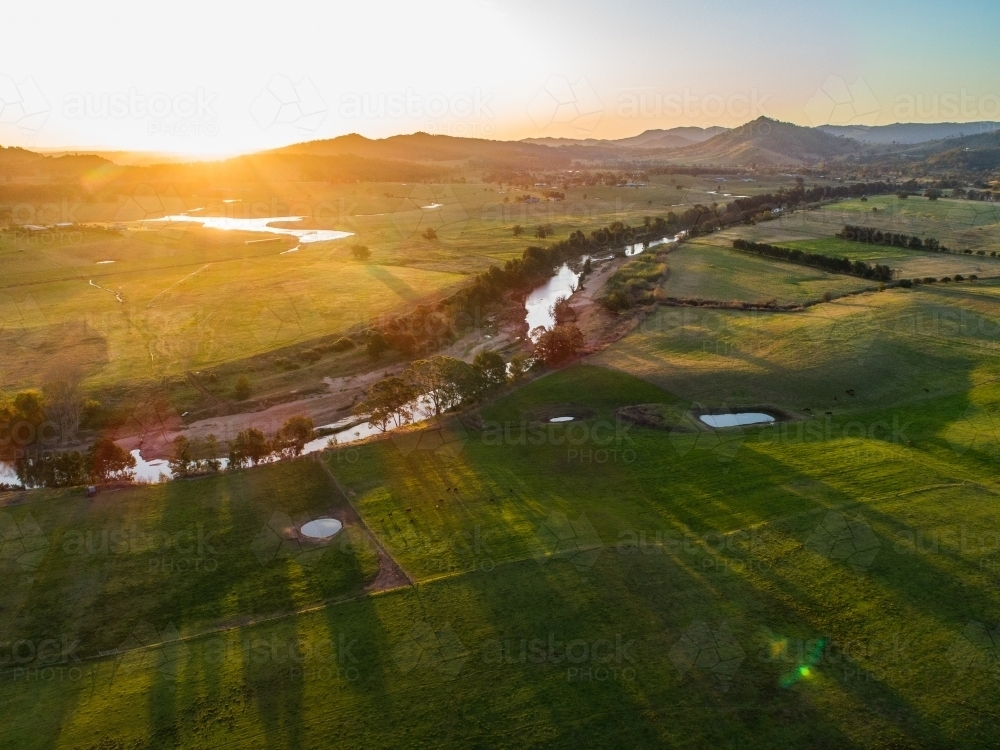 Long shadows cast over farmland from trees beside hunter river at sunset - Australian Stock Image