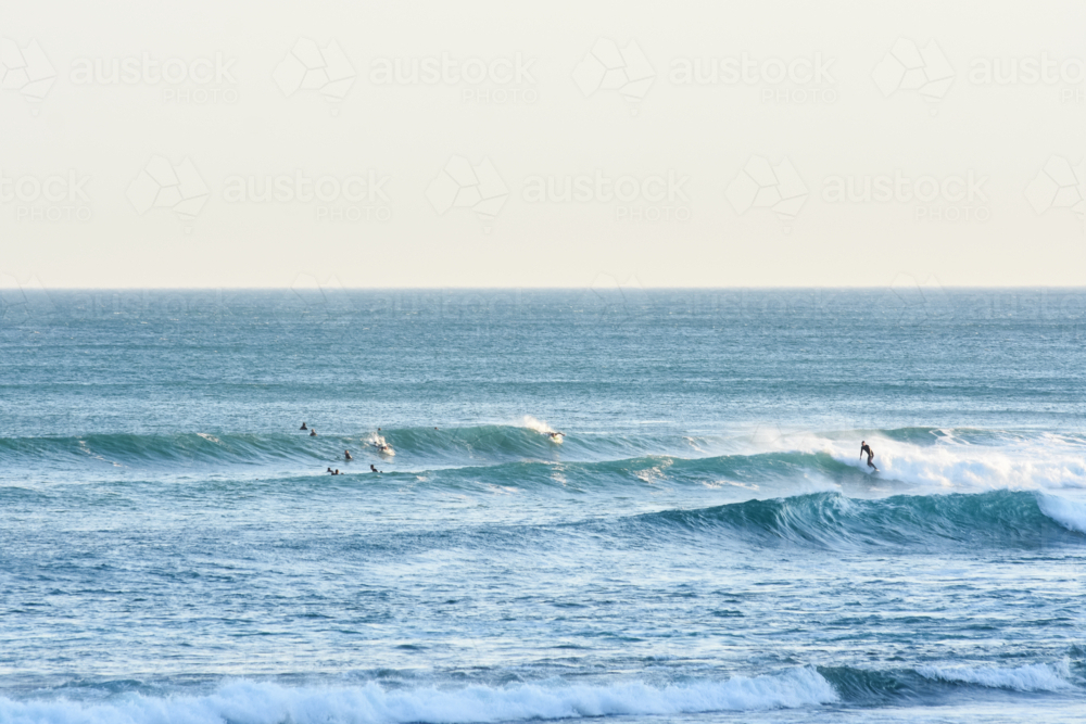 Long shot of surfers on large waves, late afternoon - Australian Stock Image